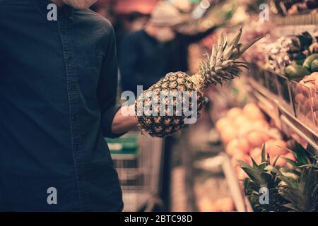 primo piano. un uomo in una maschera protettiva raccoglie un ananas maturo Foto Stock