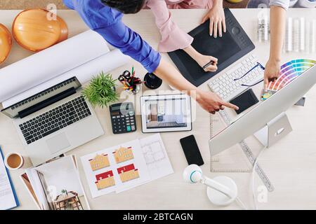 Gruppo di interior designer criticando il lavoro di collega, indicando lo schermo del computer e dando consigli su come correggerlo Foto Stock