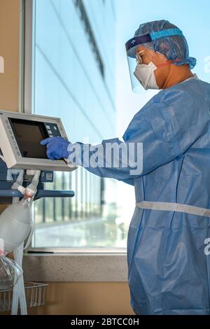 Un terapista respiratorio vestito con equipaggiamento protettivo completo in terapia intensiva regola le impostazioni del ventilatore durante la pandemia del virus corona. Foto Stock