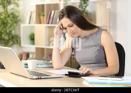 Donna di bookkeeper preoccupata che calcola sulla calcolatrice seduta su una scrivania a casa Foto Stock
