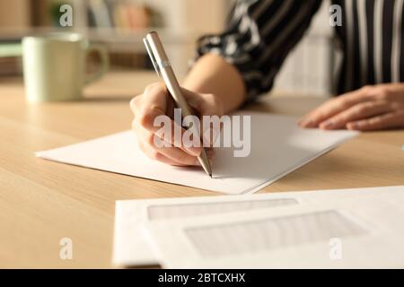 Primo piano di mani donna che scrivono lettera di notte su una scrivania a casa Foto Stock