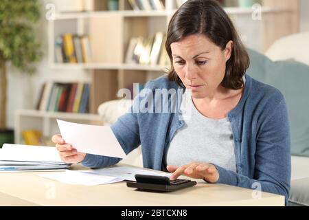 Donna adulta seria che calcola le ricevute con la calcolatrice seduta sul pavimento a casa Foto Stock