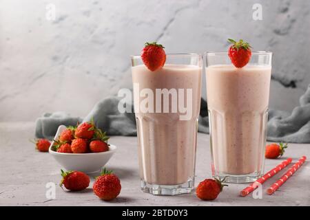 Due porzioni di cocktail proteico fatto in casa con fragole fresche e yogurt in bicchieri su fondo grigio in cemento, Dieta e controllo della perdita di peso Foto Stock