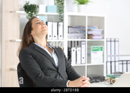 Donna dirigente felice che respira aria fresca seduto su una scrivania in ufficio Foto Stock