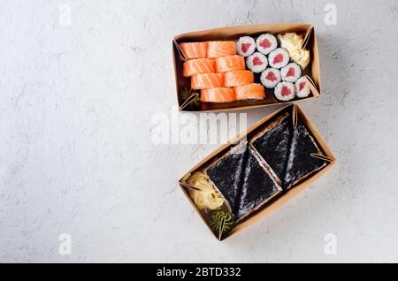 Gustosi panini di sushi in scatole di carta Kraft usa e getta, salsa su tavolo scuro. Concept servizio di consegna cibo giapponese in contenitore ecologico. Posa piatta, modello mocku Foto Stock