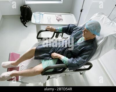 Felice uomo senior sorridente - vista elevata di sdraiarsi sulla sedia medica maschio senior all'interno di ospedale moderno in Francia riposo dopo infezione virus coronavirus Foto Stock