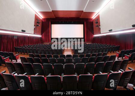 Vista grandangolare dell'interno di un cinema che mostra l'architettura e le file di posti a sedere rossi vuoti che si affacciano su un palco desertato Foto Stock