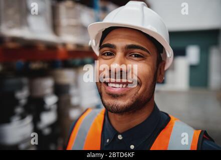 Ritratto di sorridente supervisore del magazzino che indossa un elmetto bianco sorridente alla telecamera Foto Stock