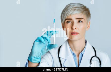 L'infermiere effettua l'iniezione. Donna in camice bianco con guanti medici guarda la siringa Foto Stock