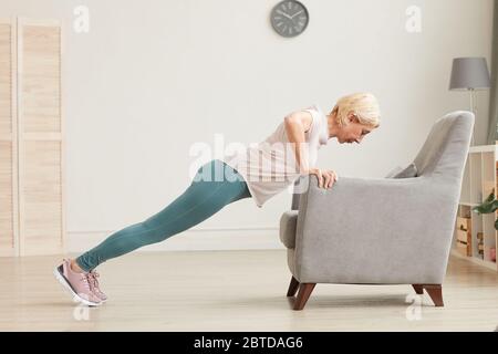 Donna anziana che fa la spinta in su usando la poltrona durante l'addestramento di sport a casa Foto Stock