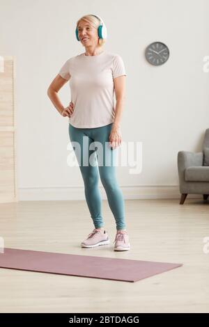 Donna anziana in cuffia che ascolta musica e pronta per l'allenamento sportivo a casa Foto Stock