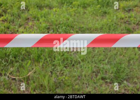 Nastro di avvertimento rosso e bianco teso su un'erba verde su sfondo sfocato. Accesso limitato al parco durante la pandemia di coronavirus. Foto Stock