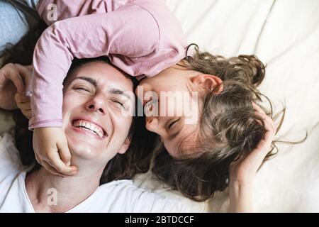 Una bambina si distende nel letto della madre mentre afferra il viso e ride. Stanno giocando molto Foto Stock