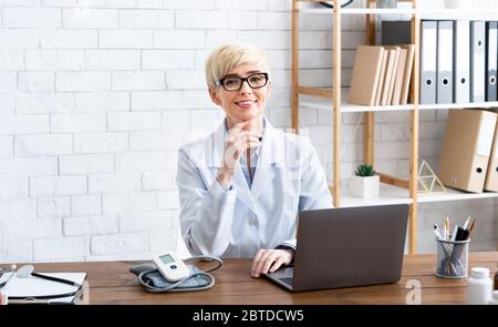 Trattamento accessibile. Donna sorridente dottore seduto al tavolo Foto Stock