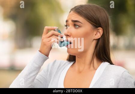 Donna che ha un attacco asmatico usando un inalatore che sta in piedi all'aperto Foto Stock