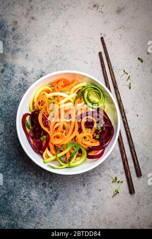 Tagliatelle vegetali - zucchine, barbabietole e carote in una ciotola, fondo scuro. Cibo vegano crudo. Foto Stock