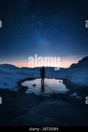 Il viaggiatore si trova in una sorgente calda segreta di notte in Islanda sotto il cielo stellato mozzafiato con la Via Lattea Foto Stock