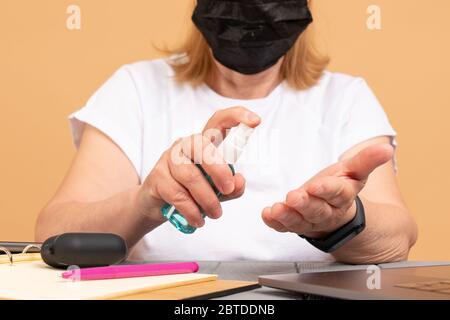 Primo piano donna anziana disinfetta le mani con disinfettante prima di lavorare con un notebook computer portatile, online formazione shopping, lavoro a casa Foto Stock