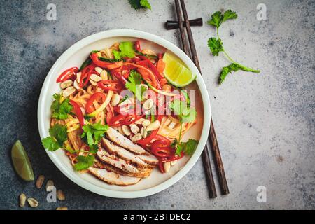 In un recipiente, a sfondo scuro, si imbottiggano noodle thailandesi con pollo, arachidi e verdure. Foto Stock