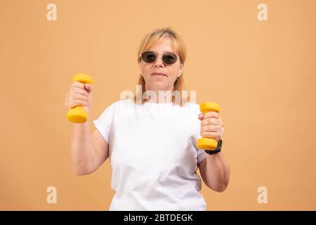 Attiva energica felice anziana caucasica femmina con capelli biondi godendo di esercizi fisici in interni, allenandosi a casa utilizzando manubri Foto Stock