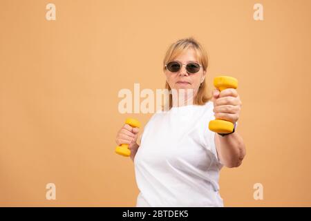 Concetto di salute, benessere, attività, maturità ed età. Donna anziana in pensione di formazione in interni, allenandosi con un paio di manubri gialli Foto Stock