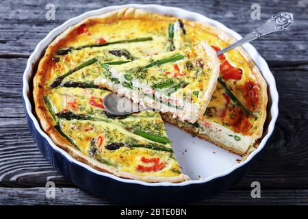 primo piano di quiche con asparagi di salmone ripieno tagliato a fette in una teglia su un vecchio tavolo di legno, vista orizzontale dall'alto Foto Stock