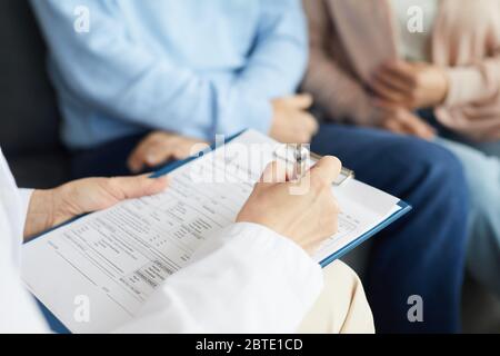 Primo piano di femmina medico che scrive sulla clipboard mentre consultando unriconoscable coppia matura in clinica, spazio di copia Foto Stock