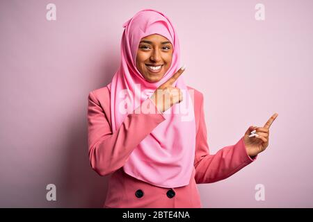 Giovane afro afro africano americano donna con hijab musulmano su isolato sfondo rosa sorridente e guardando la fotocamera che punta con due mani e pinna Foto Stock