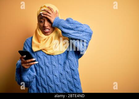 Giovane afro afro afro africano americano indossando hijab musulmano con smartphone stressato con la mano sulla testa, scioccato con vergogna e sorpresa viso, arrabbiato e fr Foto Stock