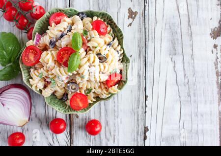 Vista dall'alto della Pasta Salad con basilico appena tritato, pomodori, olive nere, cipolla rossa e formaggio Feta, tostate con un condimento all'olio italiano. Foto Stock