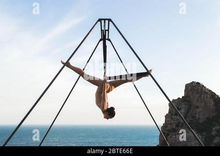 Donna che pratica la danza della mosca la gravità yoga pone in un amaca sulla costa con vista sulle montagne Foto Stock