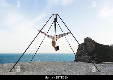 Donna che pratica la danza della mosca la gravità yoga pone in un amaca sulla costa con vista sulle montagne Foto Stock