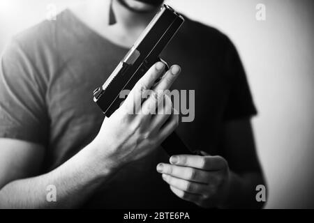 Immagine in bianco e nero di un uomo in una t-shirt che tiene una pistola e la sostituisce con una rivista con cartucce. Pericolo. Esercito. Killer. Foto Stock