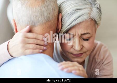 Primo piano ritratto di elegante donna anziana abbracciando il marito mentre cerca di confortarlo o sostenerlo con gli occhi chiusi Foto Stock