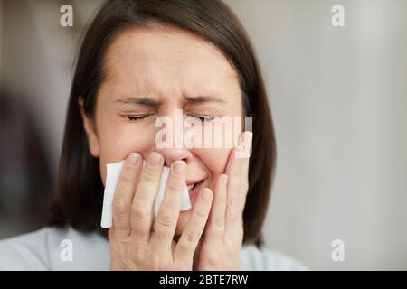 Primo piano ritratto di una donna adulta frustrata piangendo istericamente con gli occhi chiusi e tenendo tessuto, copia spazio Foto Stock