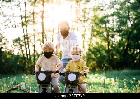 Padre con due bambini piccoli e maschere di fronte in bicicletta viaggio in natura. Foto Stock