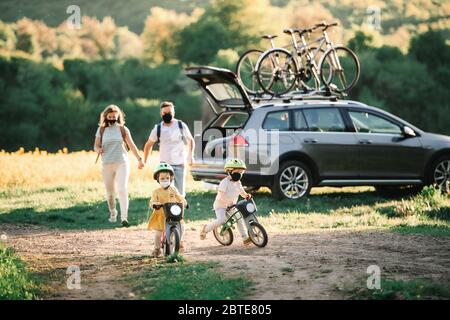 Famiglia con due bambini piccoli e maschere di protezione in viaggio in bicicletta in campagna. Foto Stock