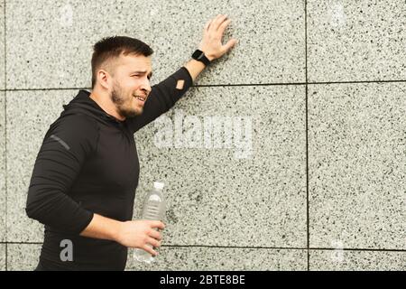 Uomo esausto appoggiato a parete dopo un lungo periodo fuori Foto Stock