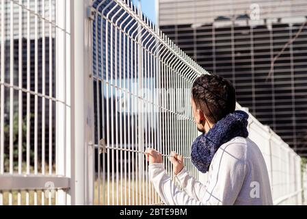 Giovane maschio appoggiato su una recinzione metallica mentre si guarda lontano agli edifici commerciali Foto Stock