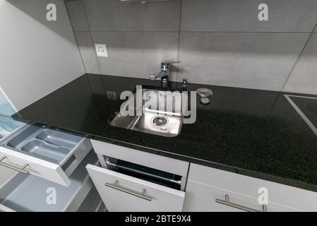 Una vista interna di cucina semplice e moderna in grigio e bianco con piano di lavoro in pietra nera Foto Stock