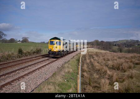 Freightliner classe 66 locomotiva 66596 passando Borwick sulla panoramica linea ferroviaria rurale poco nord-ovest con un treno di ingegneri Foto Stock