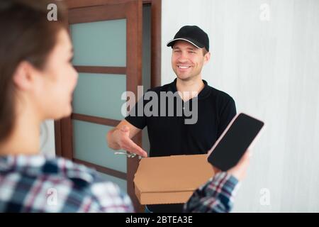 Concetto di consegna di cibo. L'uomo di consegna di cibo ha portato il cibo a casa a giovane donna. Desidera pagare l'ordine utilizzando le applicazioni dello smartphone Foto Stock