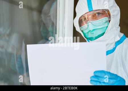 Operatori di controllo delle malattie in indumenti protettivi sulla porta con segno vuoto a causa della pandemia di Covid-19 Foto Stock