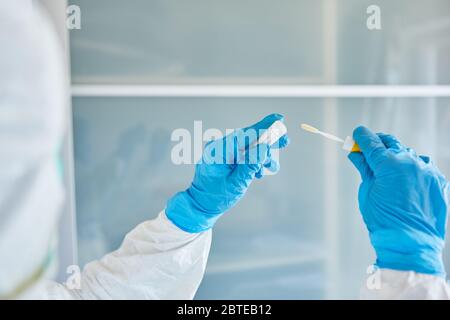 Medic in indumenti protettivi impacchi tampone per la gola per il campione di saliva durante il test del coronavirus Foto Stock