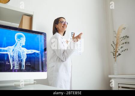 Vista laterale ritratto di un'oftalmologista sorridente che punta alla mappa durante il test oculare in clinica, spazio di copia Foto Stock