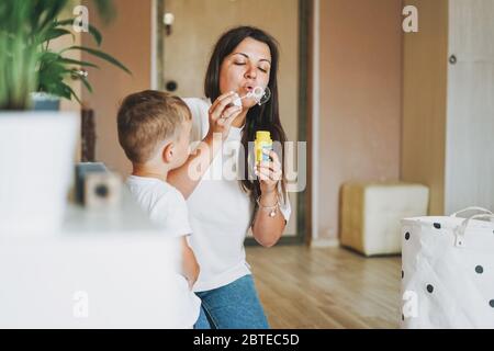 Bambino cute con la madre che soffia le bolle del sapone a casa Foto Stock