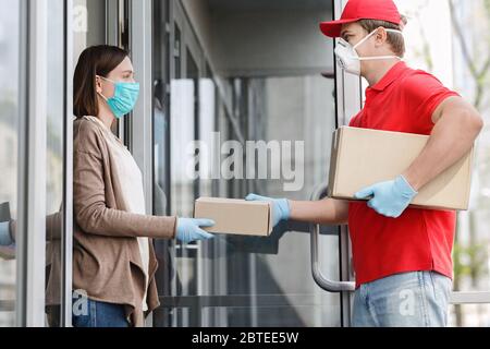 Corriere in maschera medica e guanti dà scatola al cliente, sul portico Foto Stock