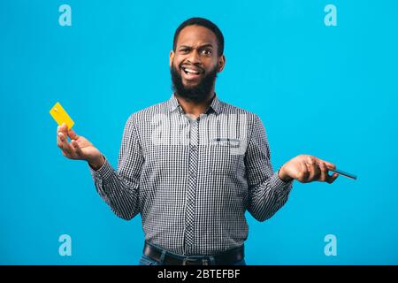Un ragazzo afro perplesso che detiene carta di credito e smartphone Foto Stock