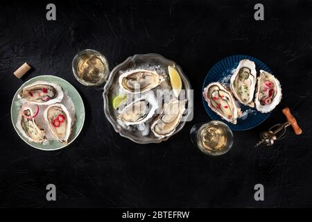 Ostriche con vari condimenti, sparate dall'alto, con limone e lime, pepe, cipolla, su fondo nero con un posto per il testo Foto Stock