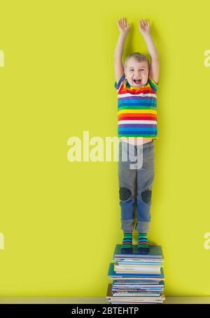 Un bambino sorridente gioioso sta in piedi su una pila di libri per bambini. Sfondo verde. Foto Stock